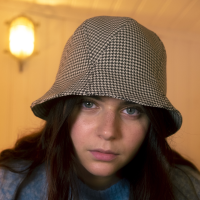 Michetti is wearing a Le Panache Paris© bucket hat made in France with Go Couture_61138, Gabriel© brand fabric, 100% Trevira cs, brown houndstooth pattern on a beige background.